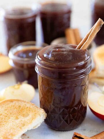 Apple butter in a mason jar. It is surrounded by sliced apples.