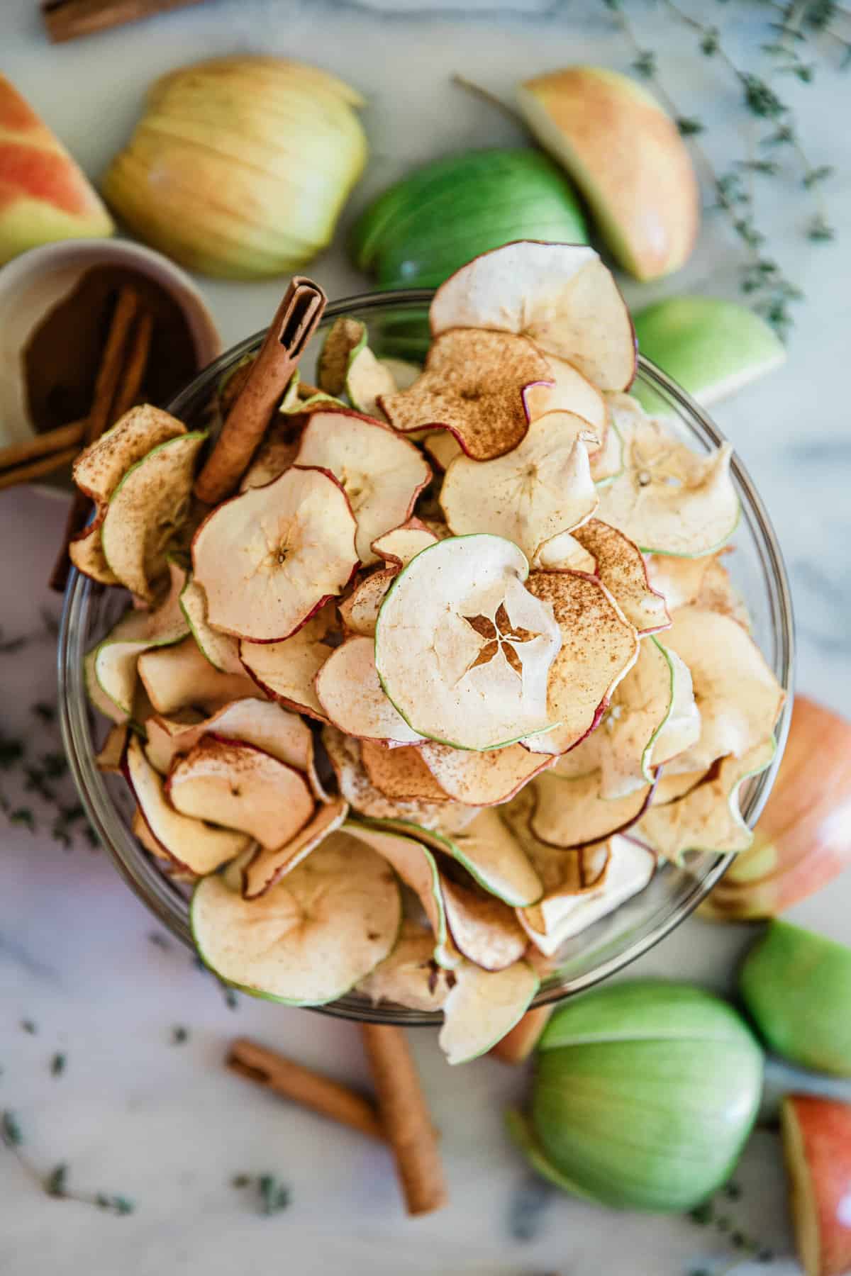 Apple chip recipe in a glass bowl. They are surrounded by sliced apples.