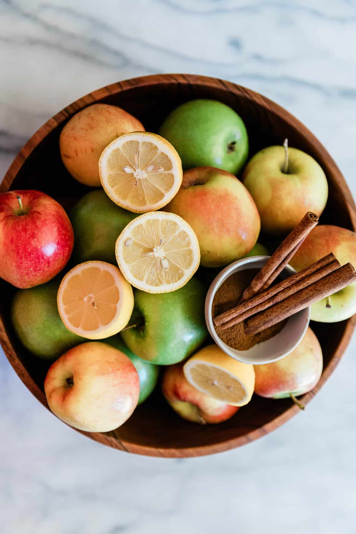 Apples, lemons, and cinnamon in a large wooden bowl.