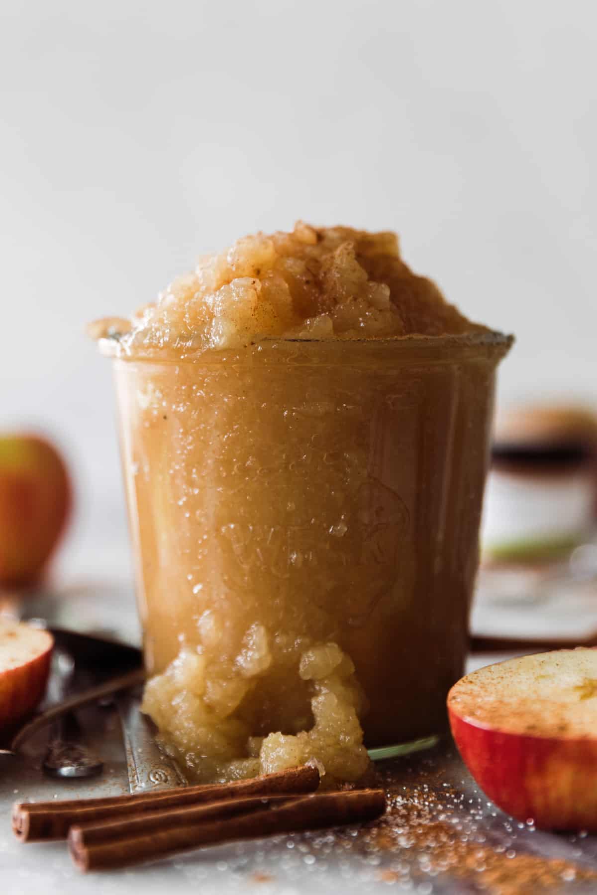 Applesauce in a jar with cinnamon sticks and apples. 