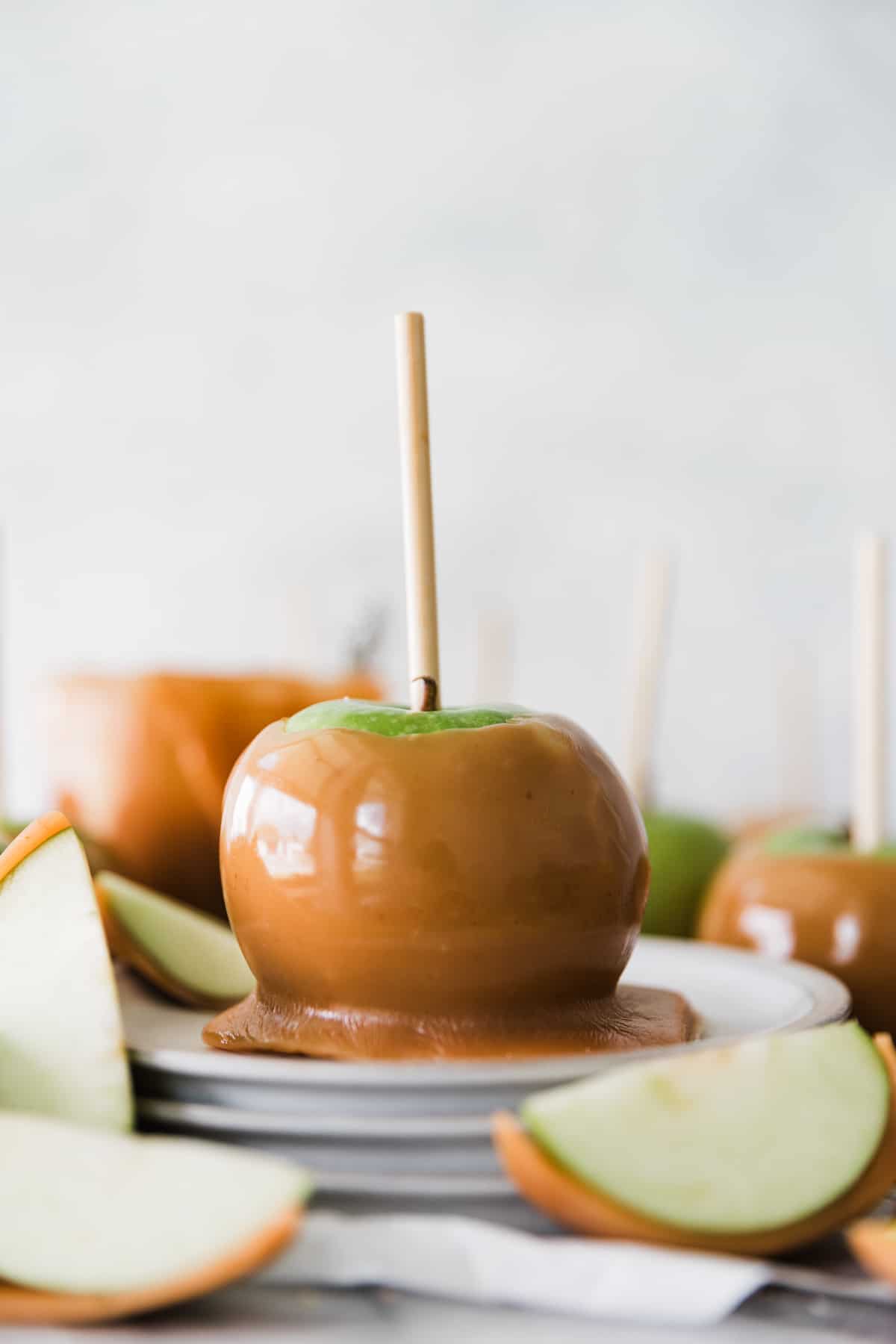 One caramel apple on a stack of plate with caramel apple slices around. 
