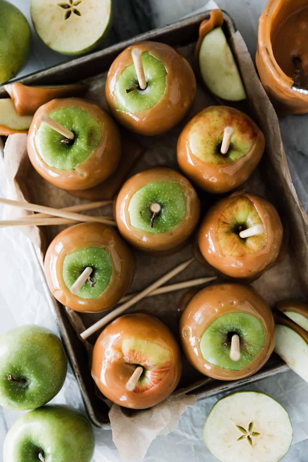 Many caramel apples on a cookie sheet resting. 