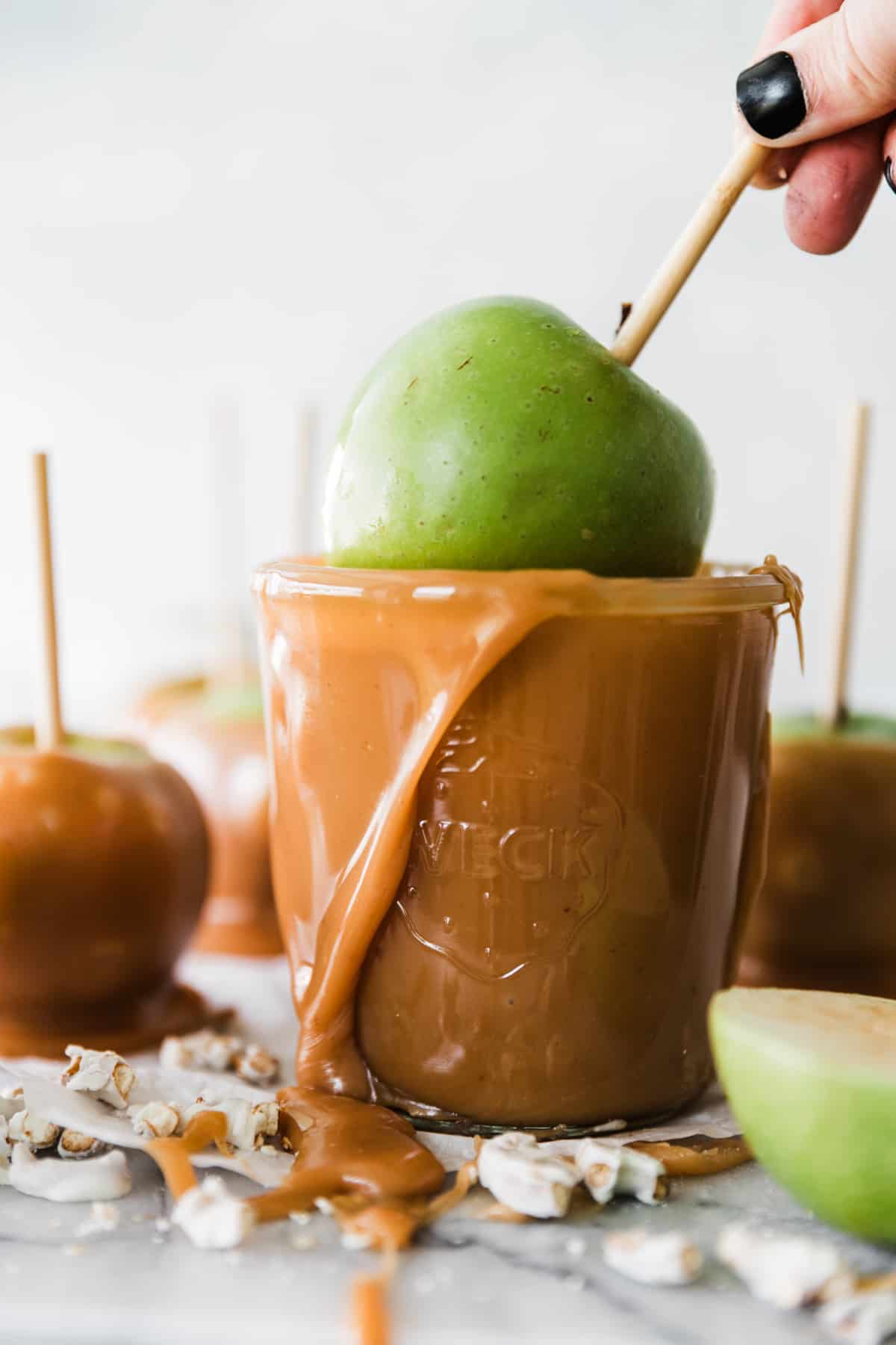 Green apple on a stick being dipped into a cup of overflowing warm sticky caramel. 