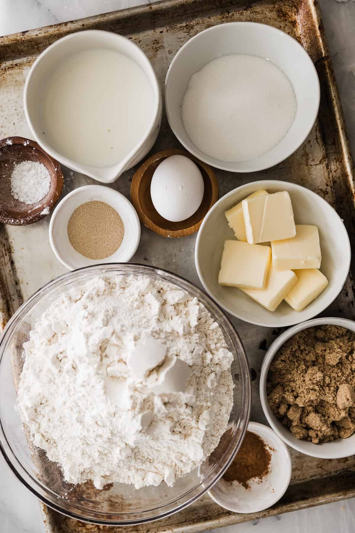 Several bowls of ingredients for cinnamon rolls on a baking tray. 