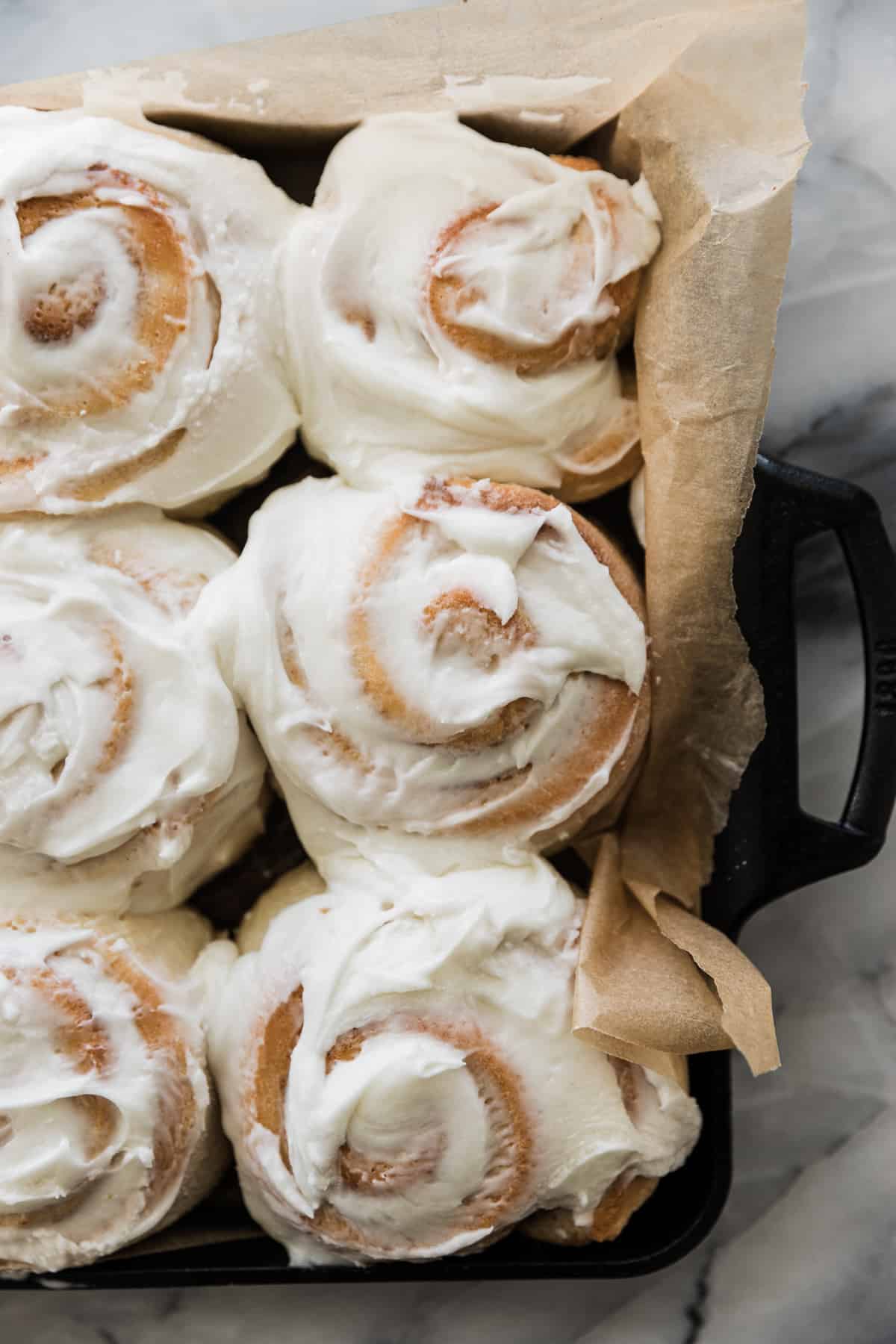 Fluffy frosted cinnamon rolls in a black pan with parchment paper. 