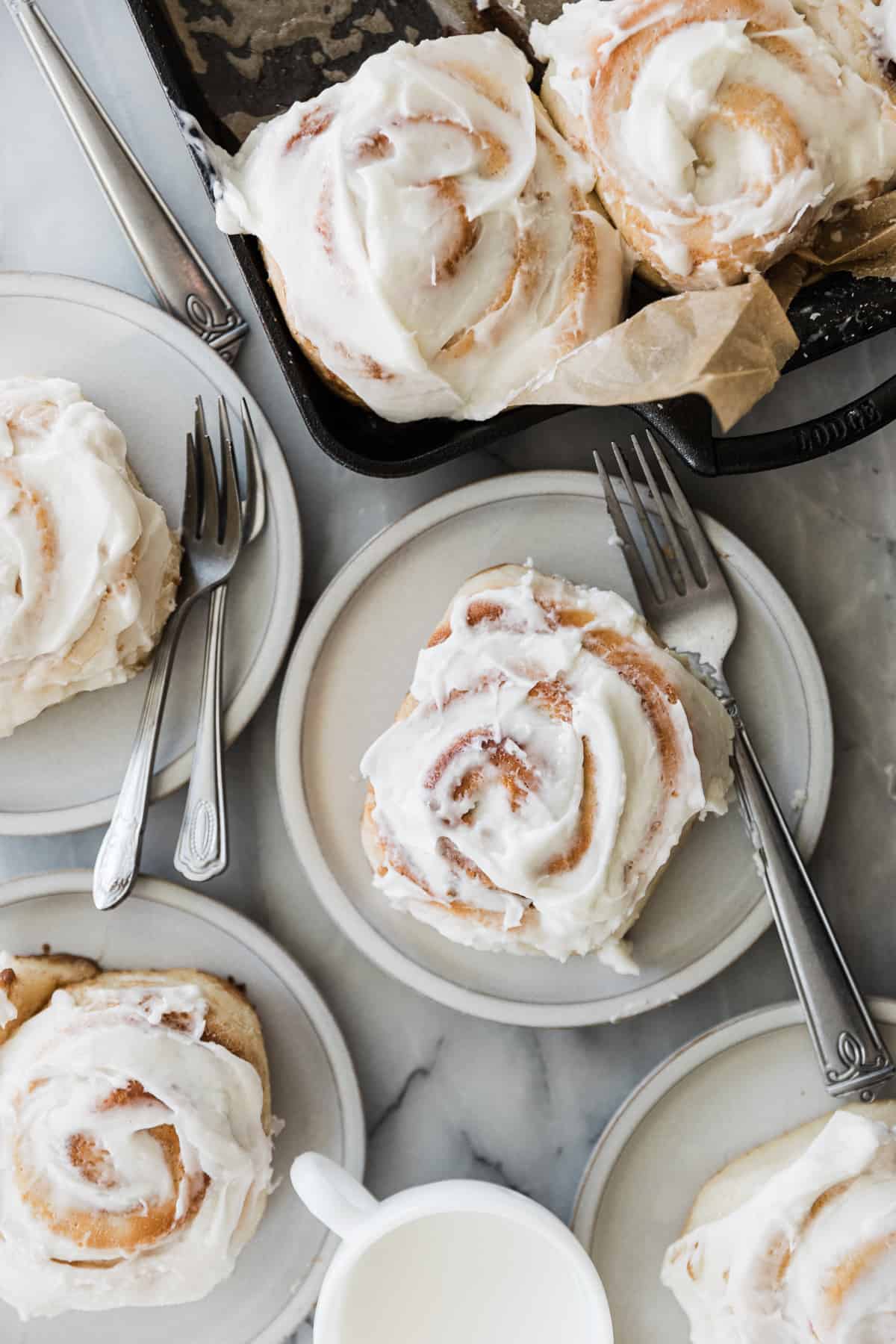 Fluffy frosted cinnamon rolls on a dessert plate with the pan next to it. 
