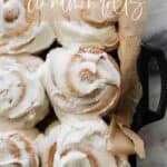 Cinnamon rolls on a black pan with parchment paper and pinterest text.