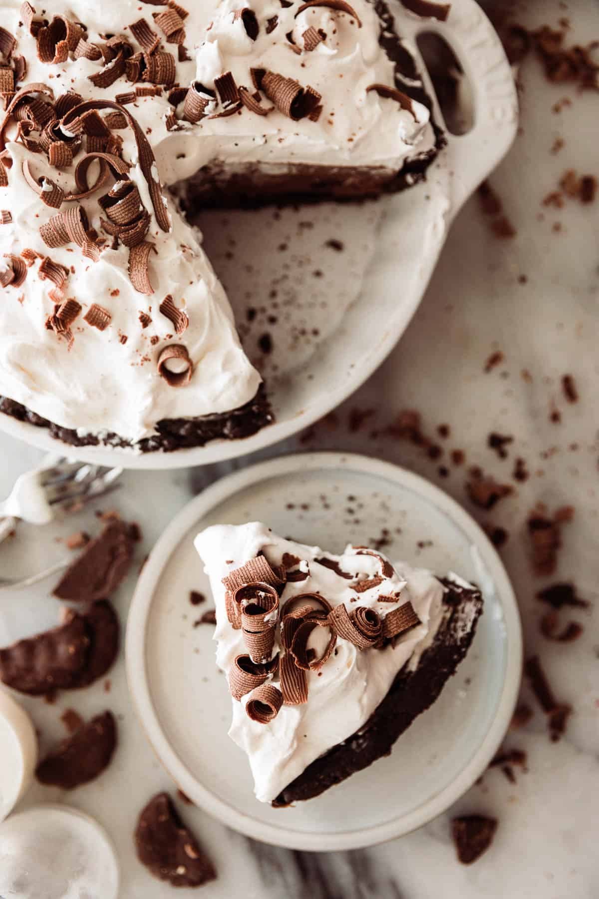 One slice of chocolate cream pie with a mint cookie pie crust on a plate and chocolate pie next to it. 