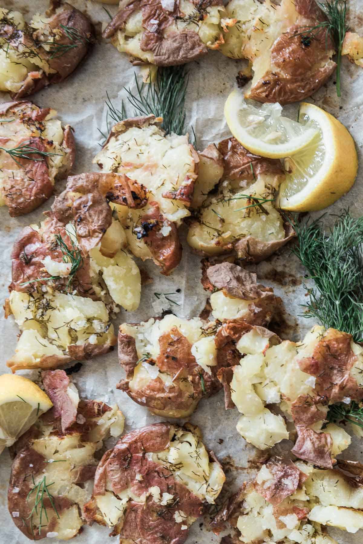 Smashed red potatoes on parchment paper. They are garnished with lemon and dill.