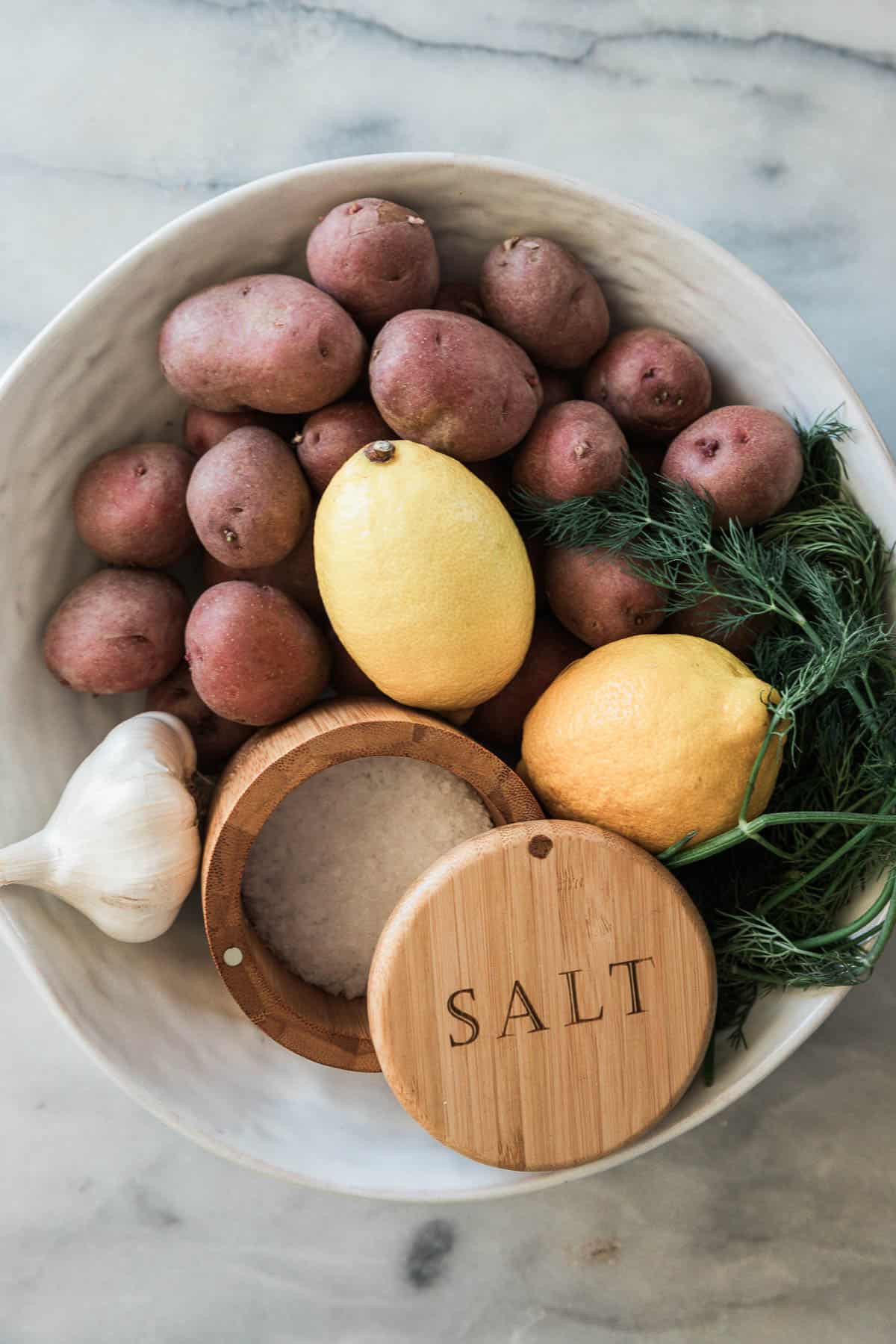 Red potatoes, lemon, dill, garlic, and salt in a white bowl.