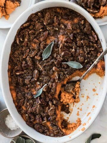 Sweet potato casserole with pecans in an oval baking dish. There is a silver spoon inserted.