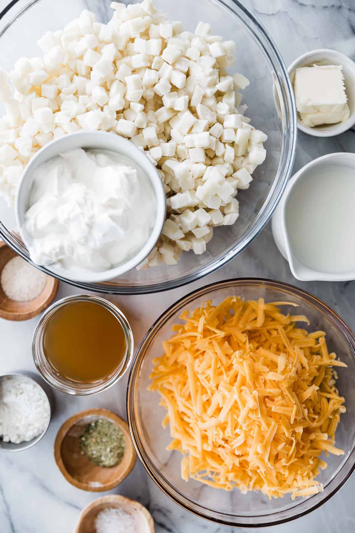 Several bowls of cheesy potato ingredients on a marble board.