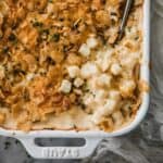 Creamy, cheesy potatoes casserole in a white dish with serving spoon.
