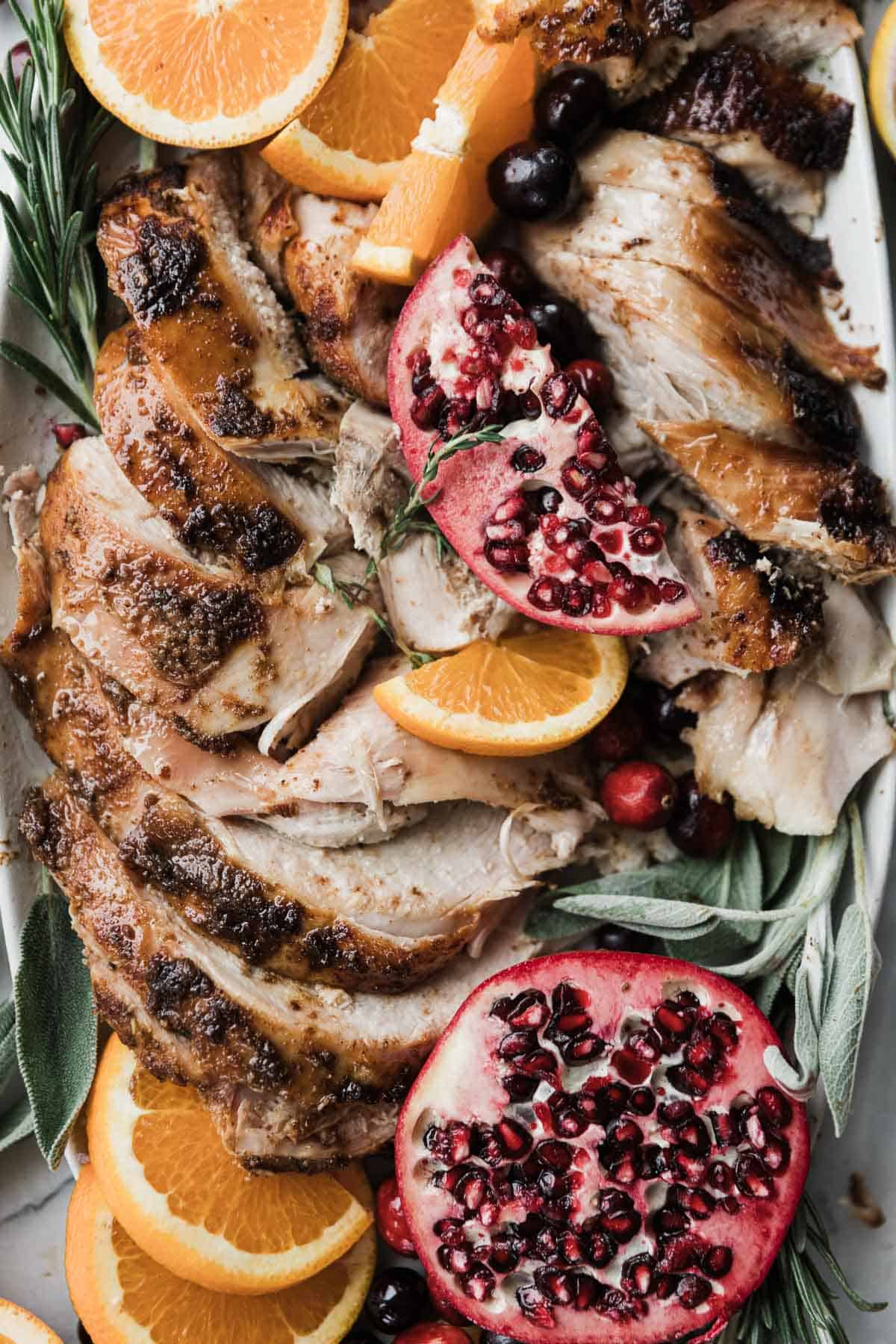 Slices of moist turkey breast on a tray with herbs and fruit. 