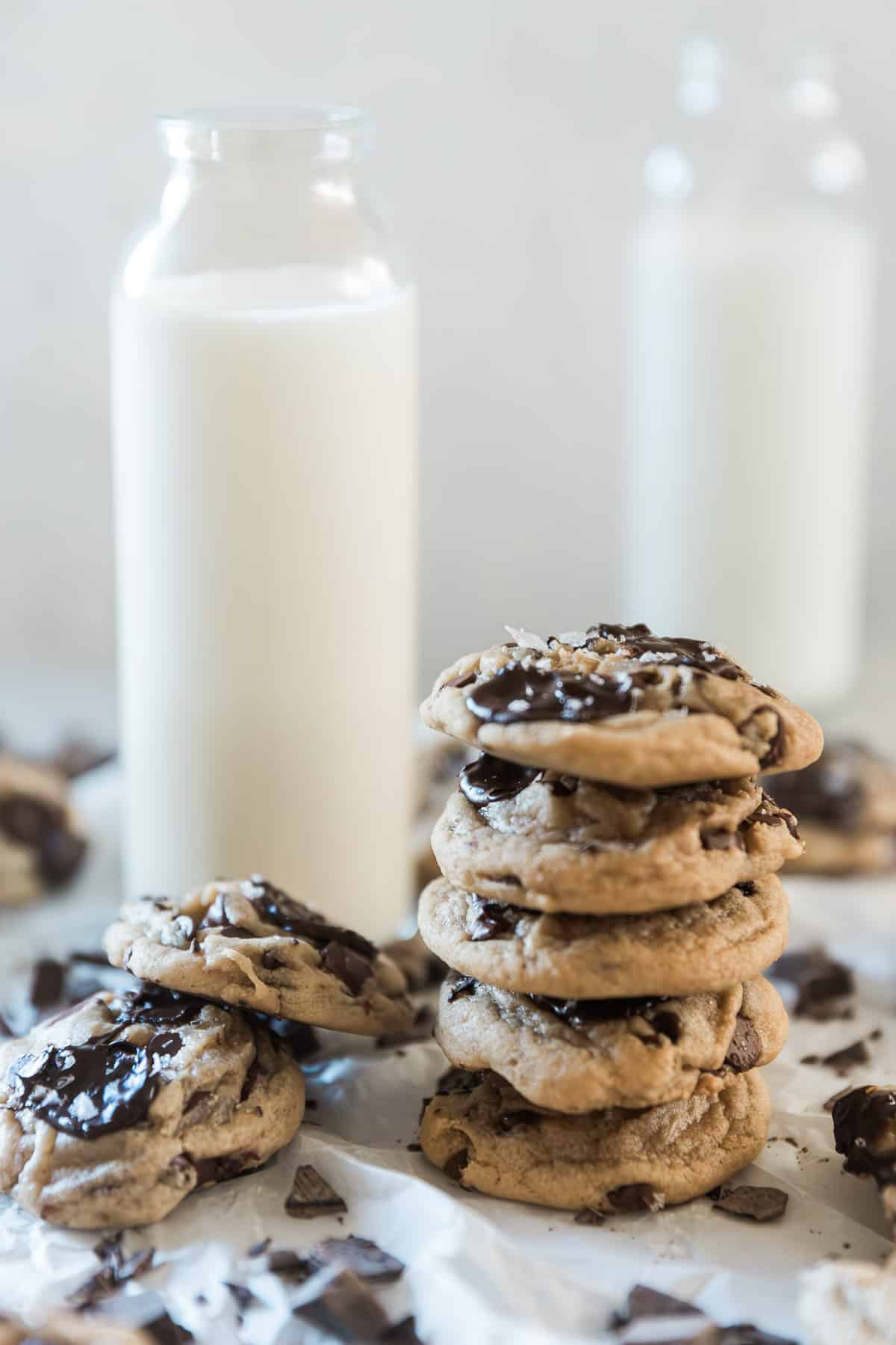 Brown butter chocolate chip cookies stacked in a pile next to a bottle of milk.