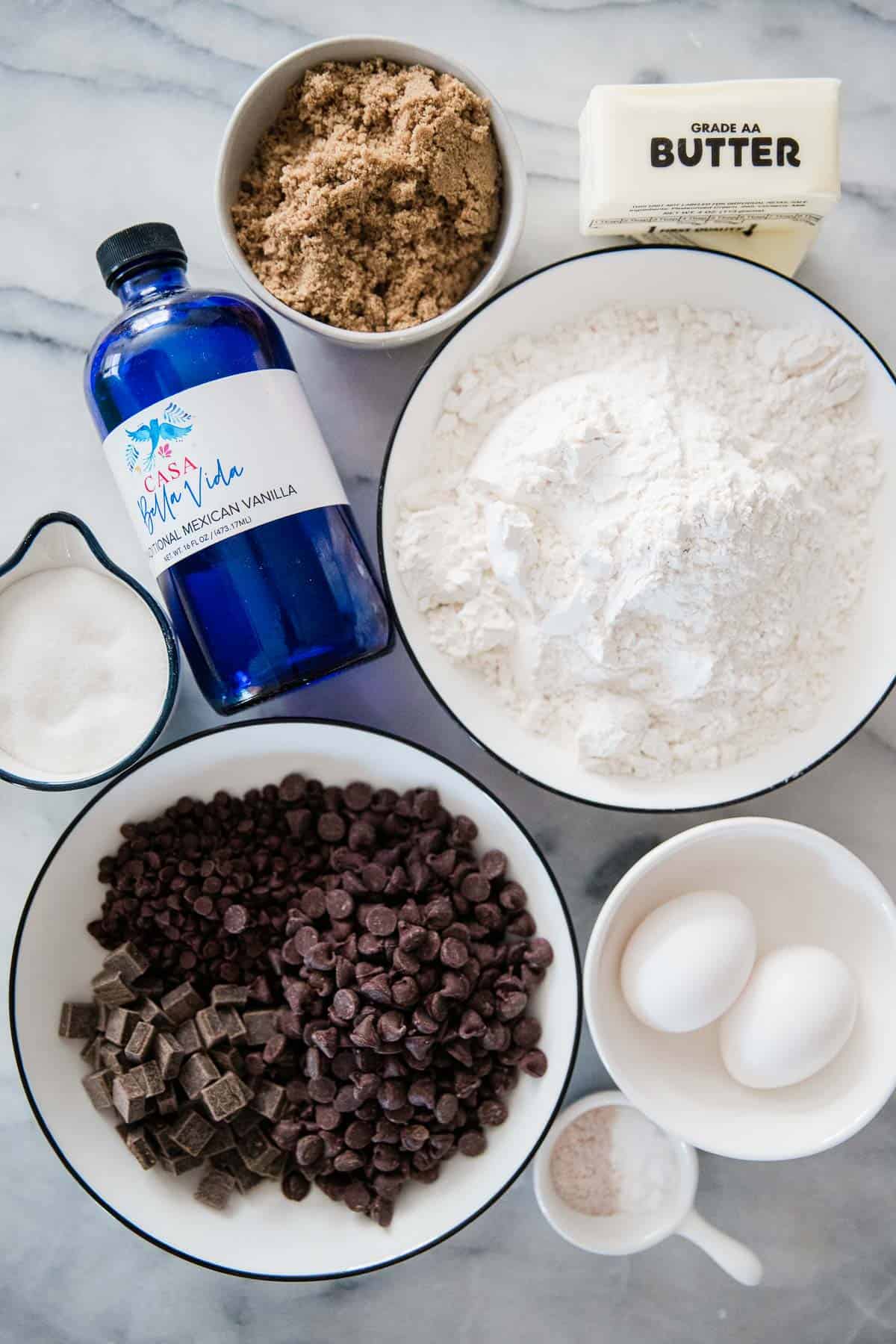 Flour, vanilla, chocolate chips, sugar, and eggs on a marble counter.