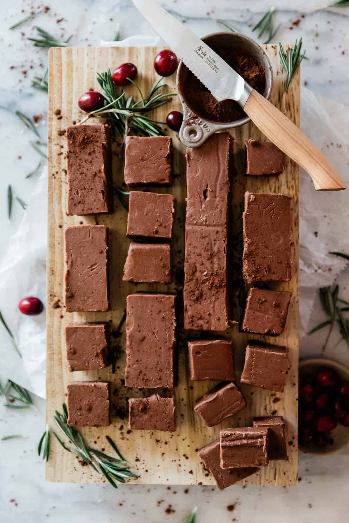 Old fashioned Hershey bar fudge cut and laid on a wooden cutting board. There are cranberries to the side.