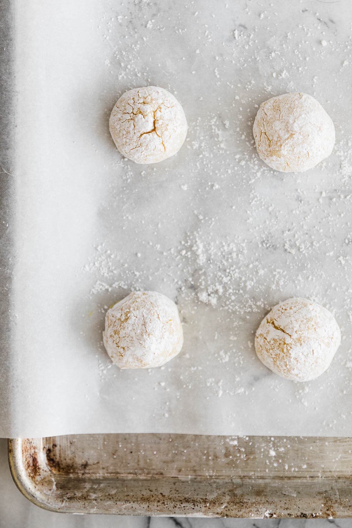 Four lemon cookie dough balls on baking sheet lined on parchment paper. 