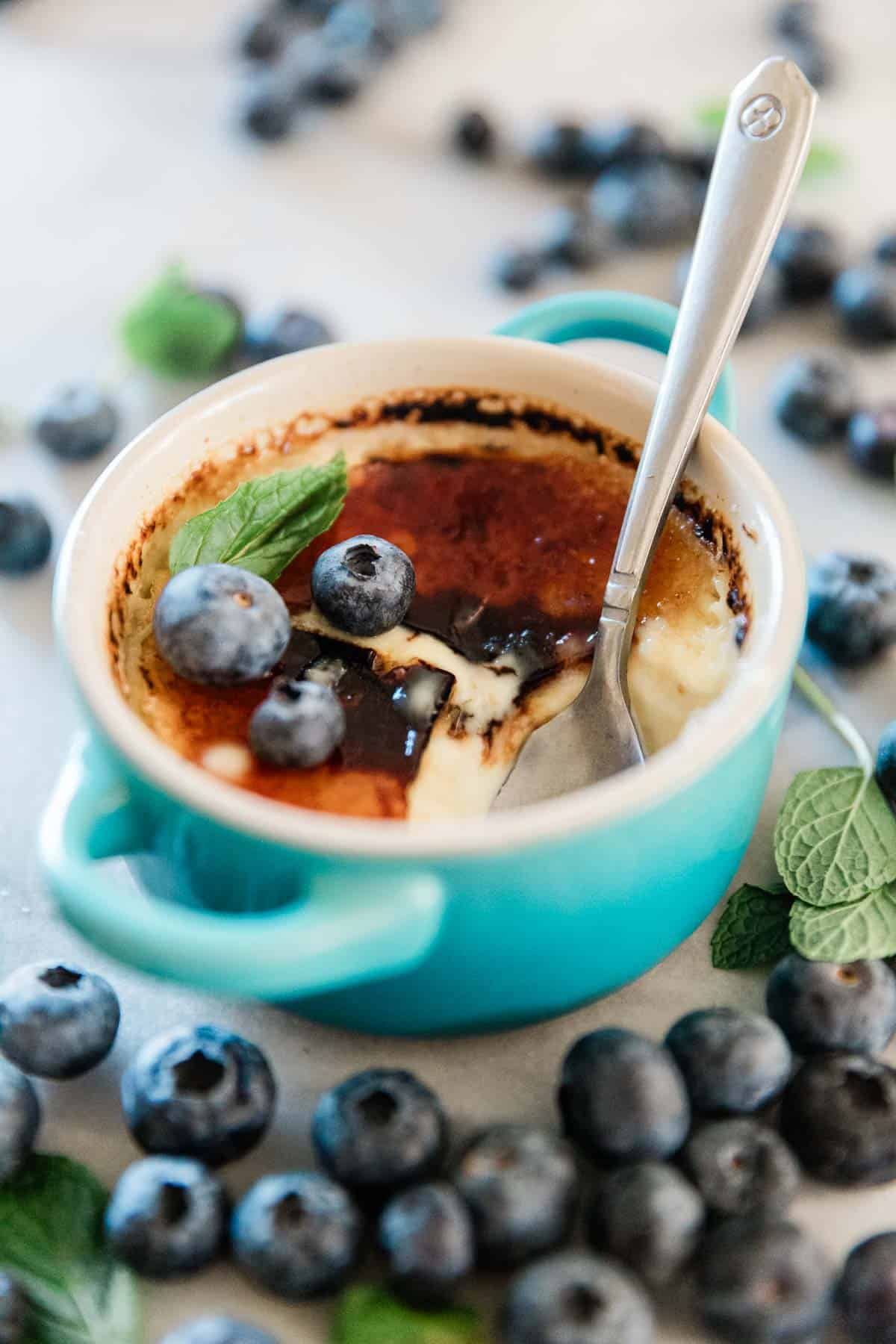 Creme brûlée in a blue ramekin. There are blueberries scattered around.