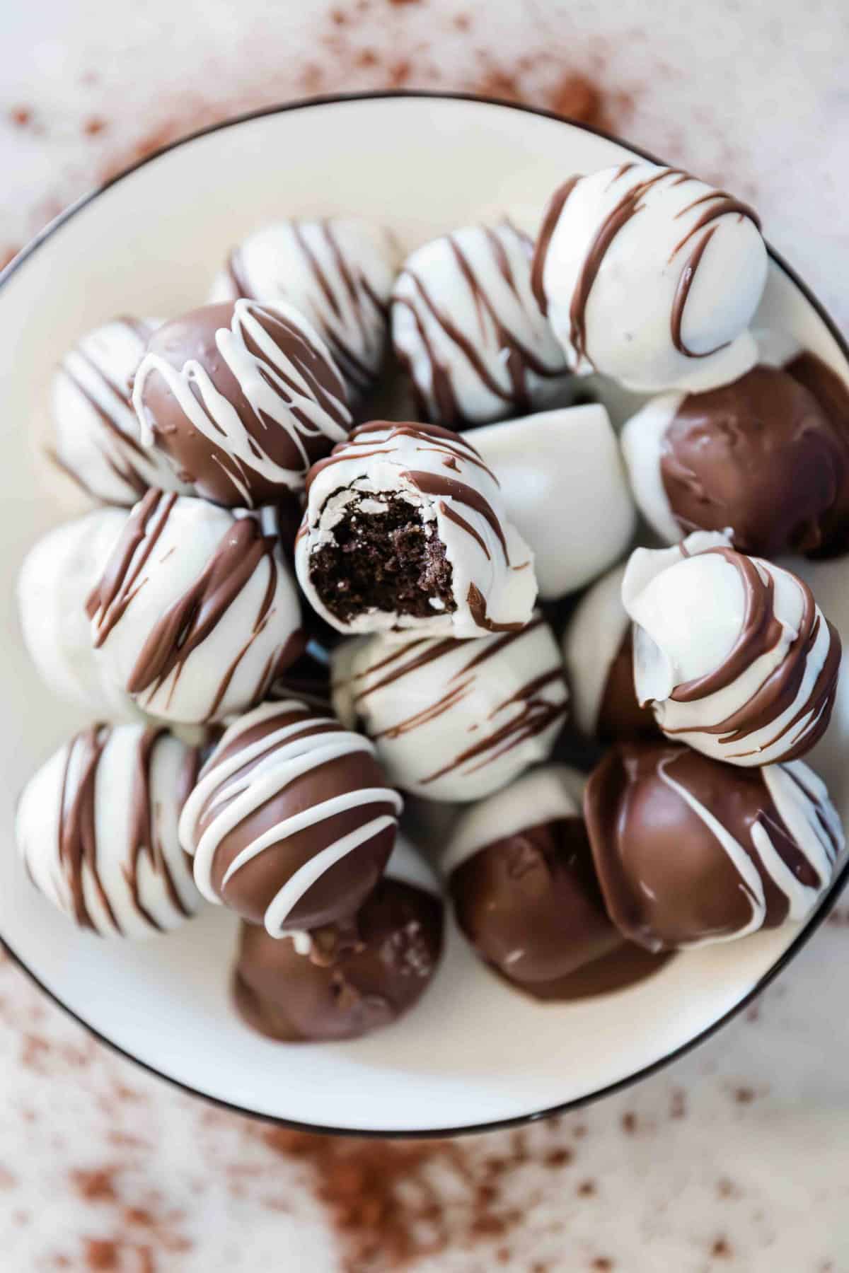 Oreo Truffles in a white rimmed bowl. There is one with a bite missing.