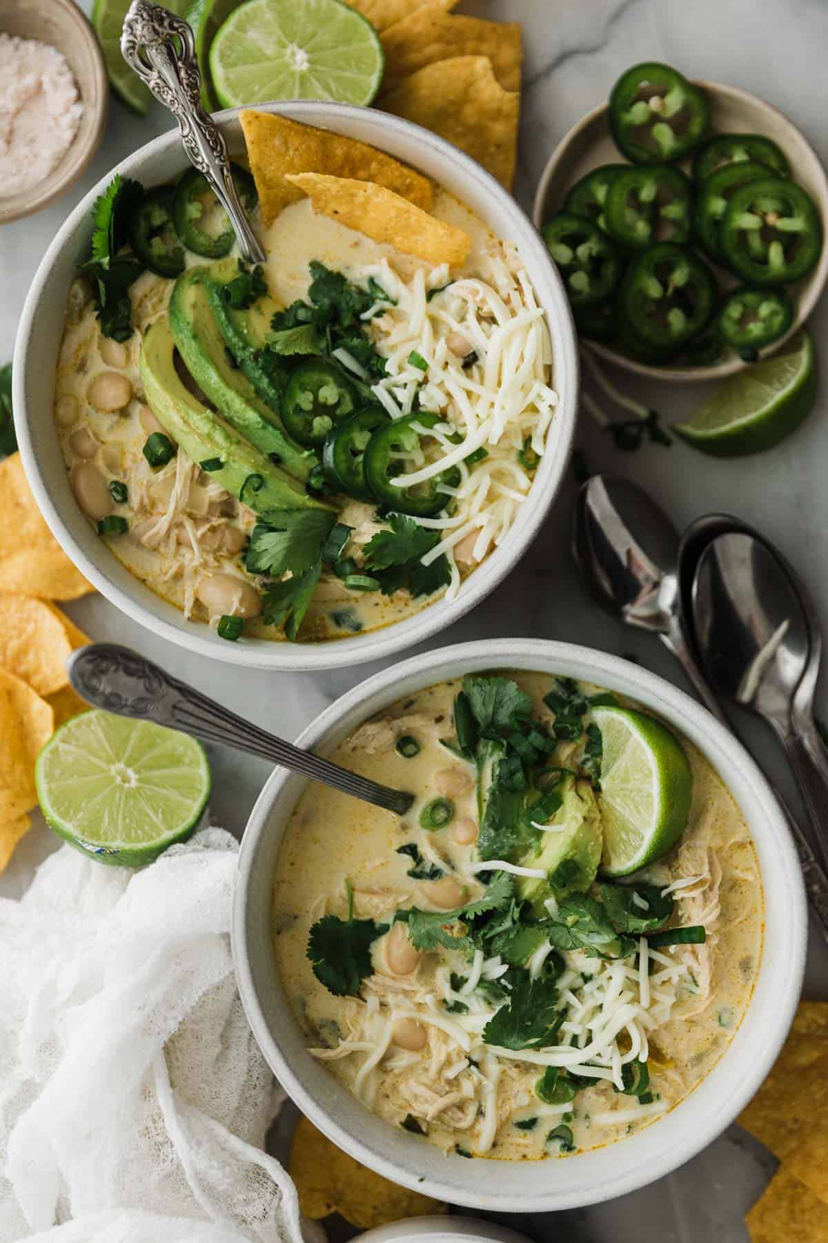 Two bowls of creamy white chili topped with lime, cilantro and avocado. 
