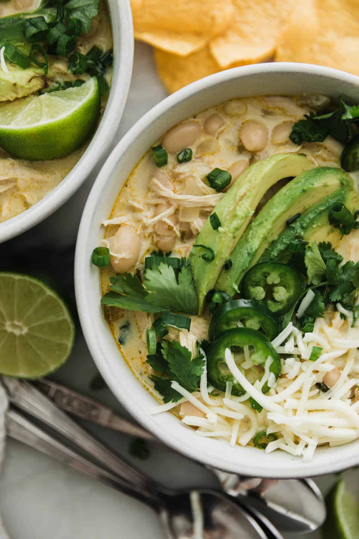 Bowl of creamy white chicken chili with avocado, cheese and garnishes. 