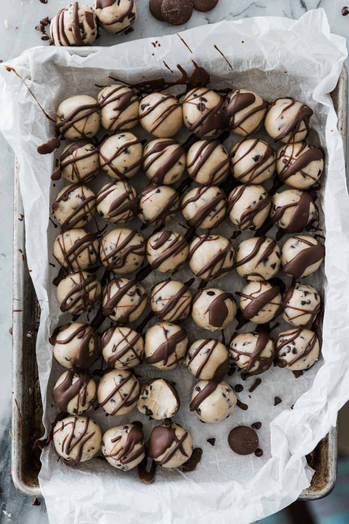 Tray of cookie dough balls with chocolate drizzled over. 