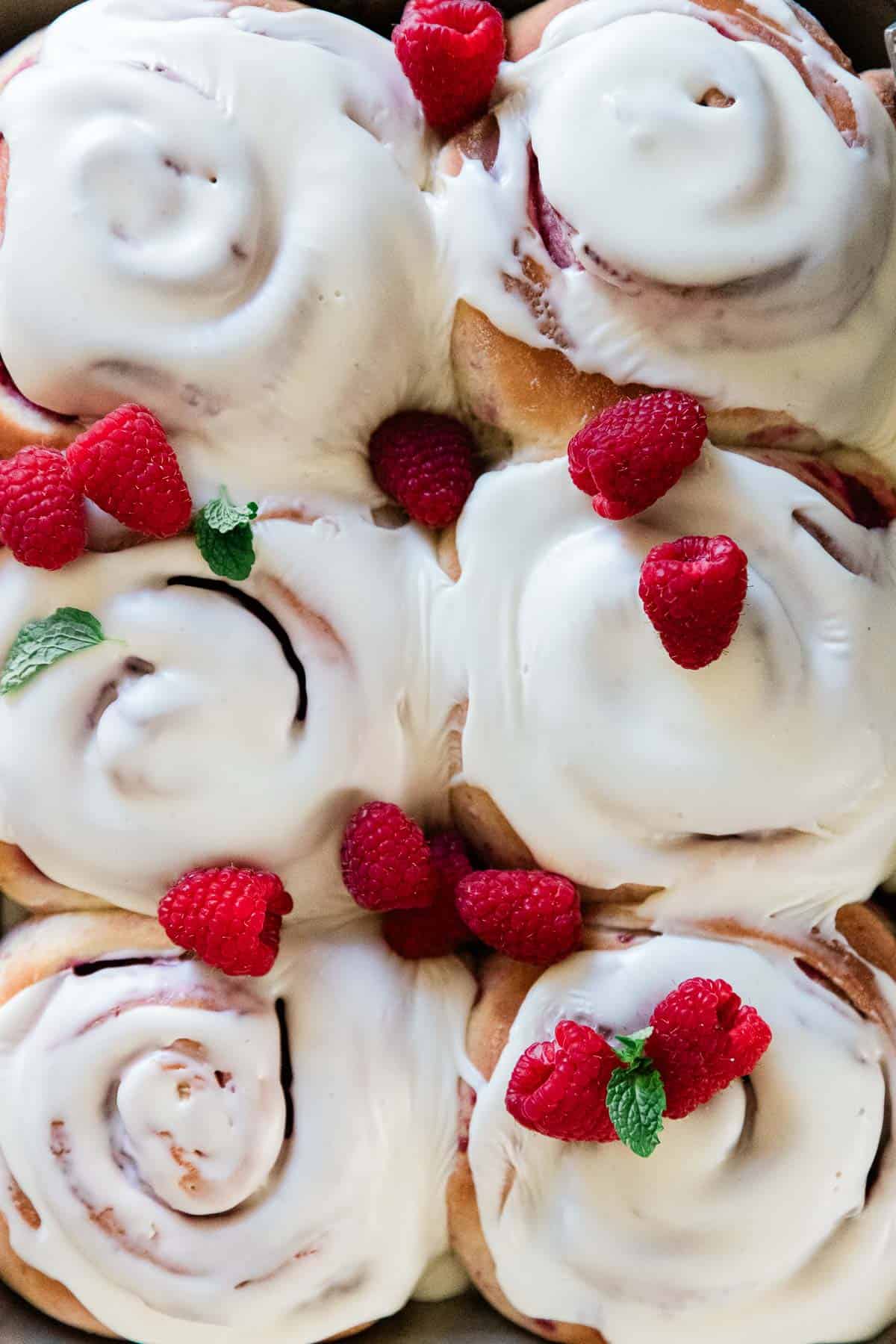 A close up of raspberry rolls frosted. They are garnished with fresh raspberries.