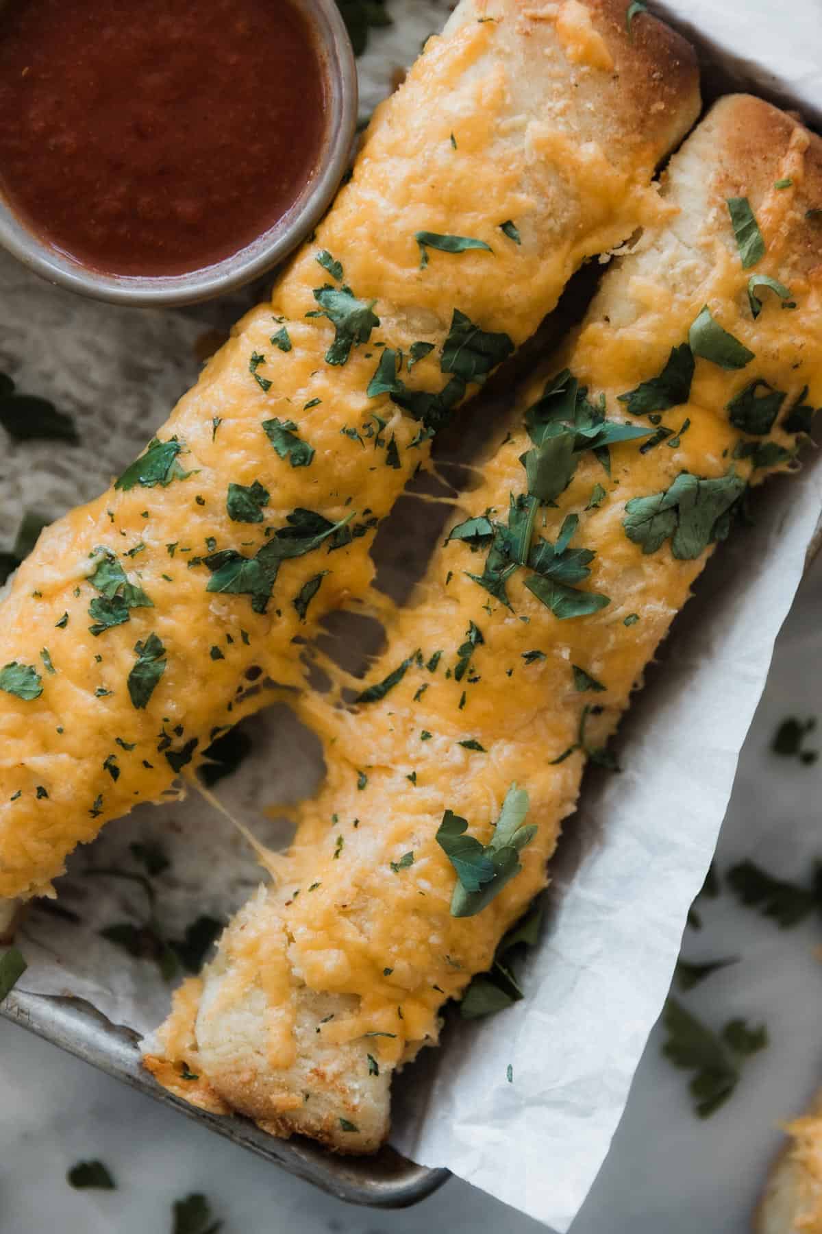 Two cheesy breadsticks with parsley and cup of marinara.