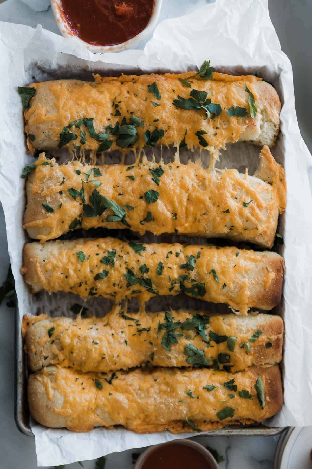 Five cheesy breadsticks with parsley and cup of marinara.
