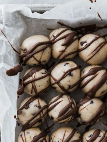 Several cookie dough bites drizzled with chocolate on cookie sheet.