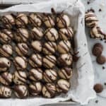 Many balls of cookie dough bites drizzled with chocolate on a baking sheet.