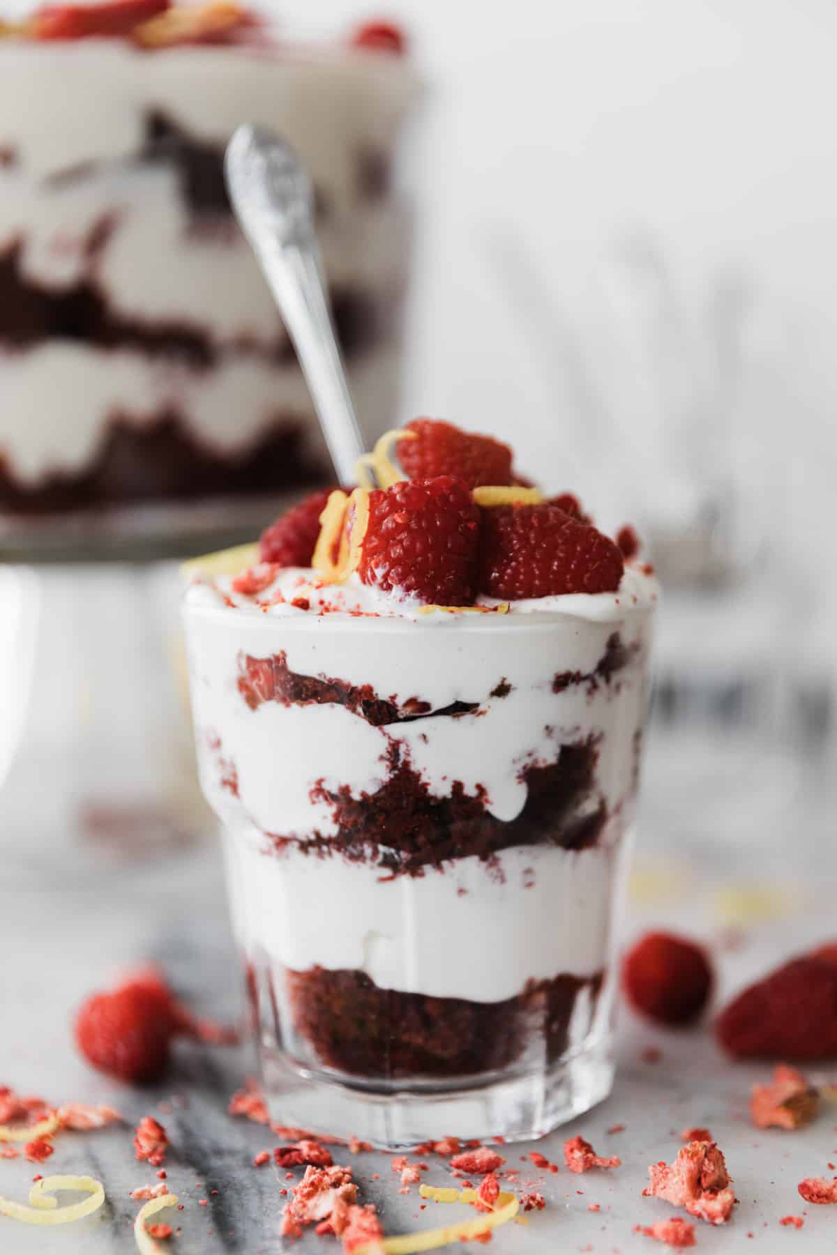 One small cup of a cream cheese red velvet trifle topped with raspberries. 