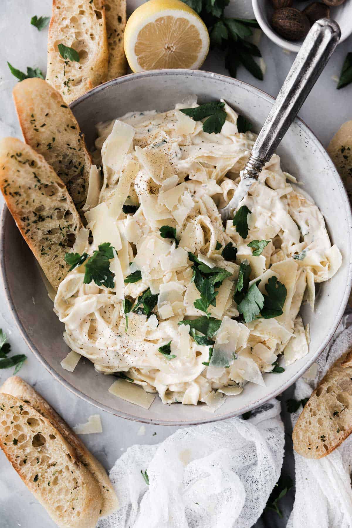 Fettuccine Alfredo in a bowl with breadsticks surrounding the bow dish. 