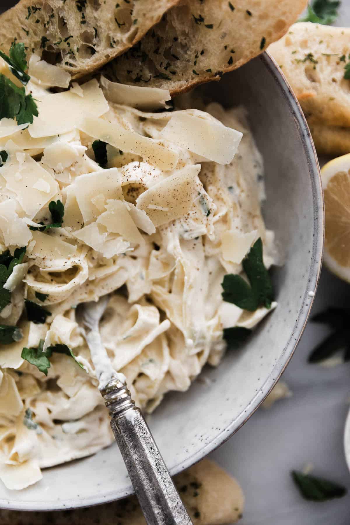 Fettuccine Alfredo in a bowl with shaved parmesan and parsley on top and a side of bread. 