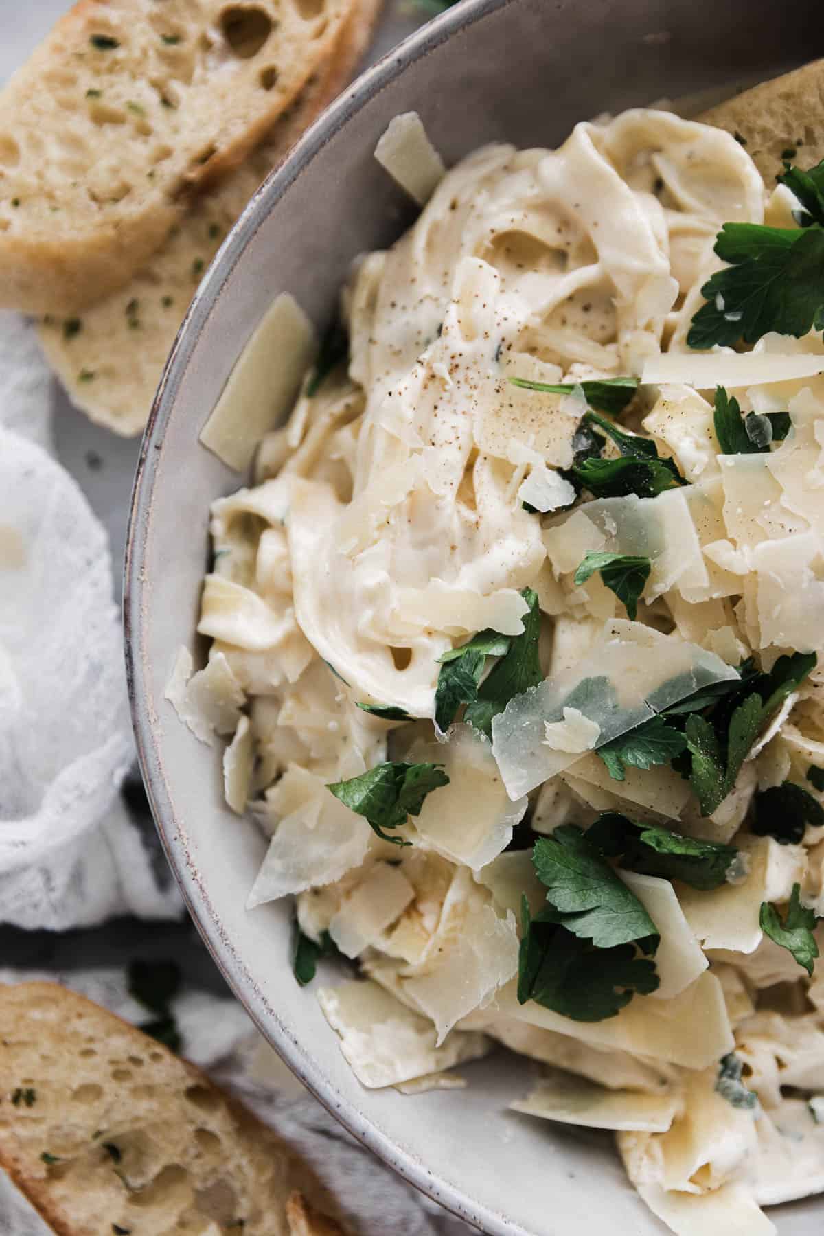 Zoomed in photo of creamy fettuccine Alfredo in a bowl with parmesan cheese and parsley. 