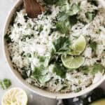 A big bowl of cilantro lime rice topped with limes and a wooden spoon.