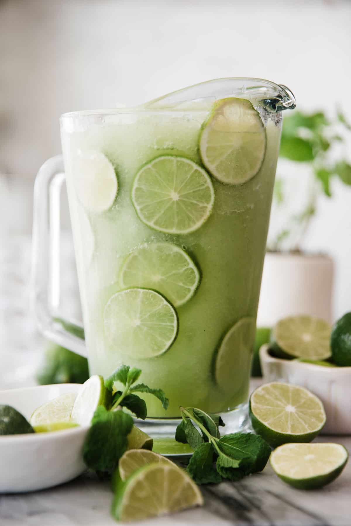 One large pitcher with lime garnish filled to the top with a frozen mojito mocktail.