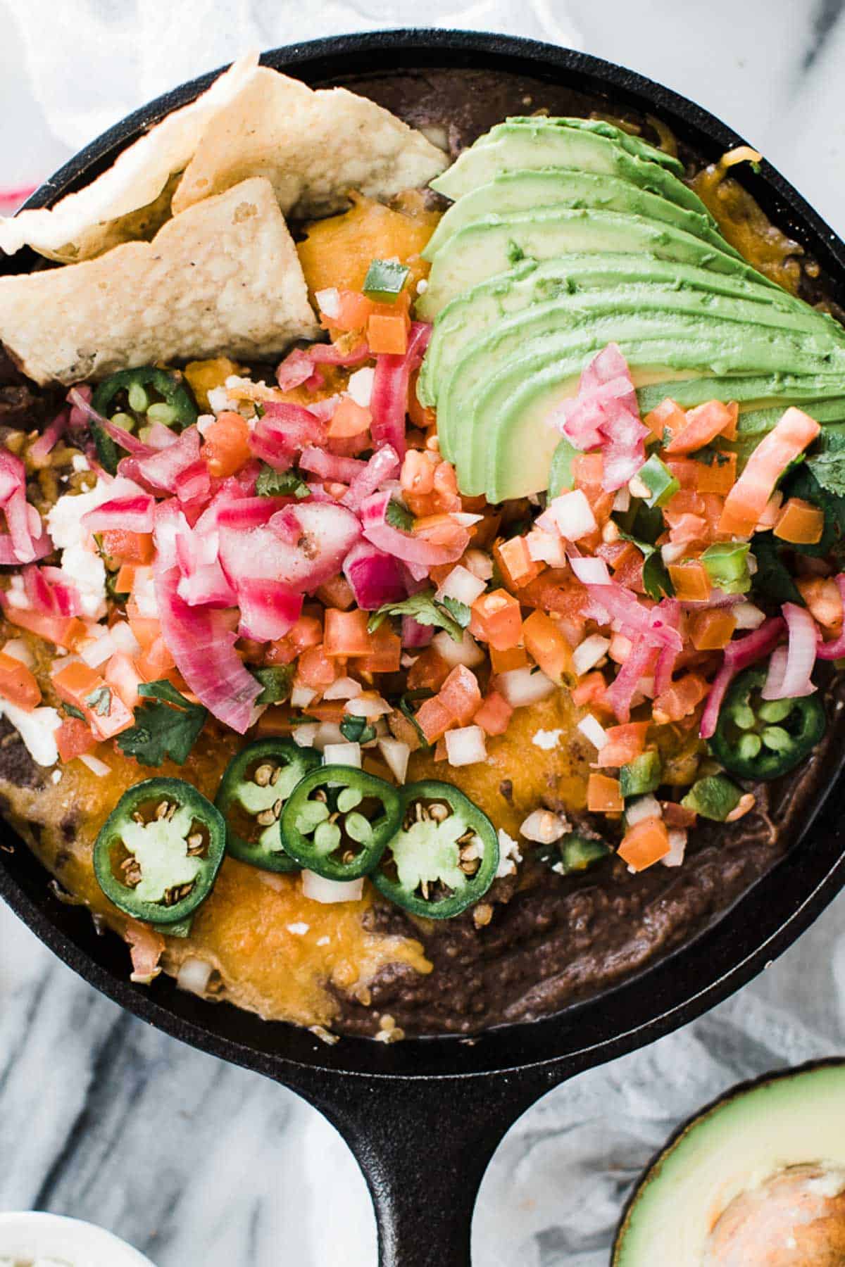 Black bean dip in a cast iron pan with melted cheese and loaded with toppings.