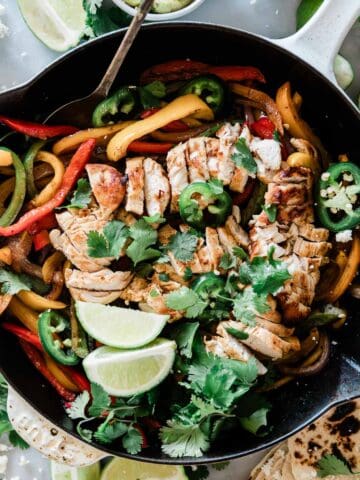 Chicken fajitas recipen a skillet. It is garnished with cilantro and jalapeños.