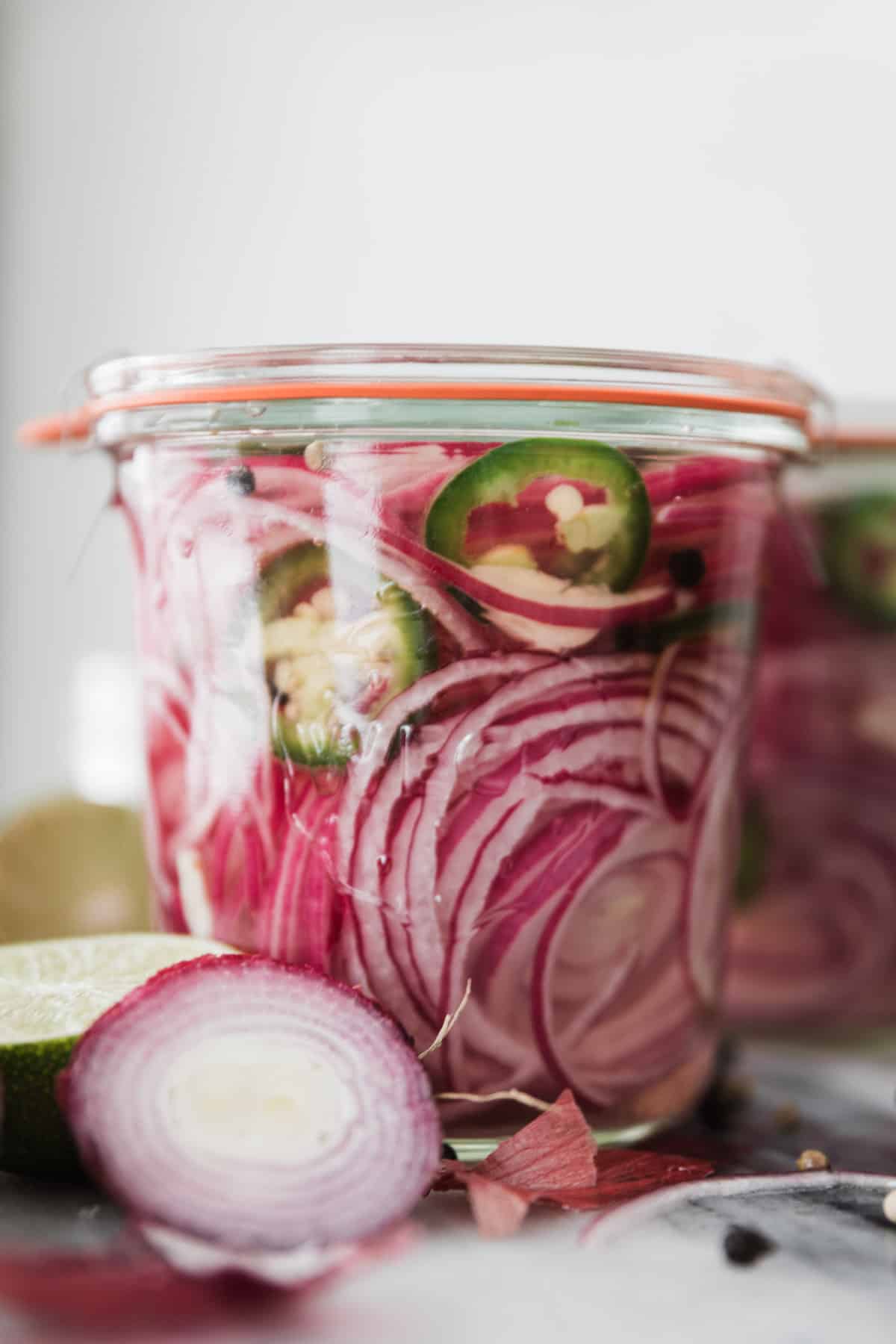 A glass jar of thinly sliced onions, spices and vinegar and sealed.
