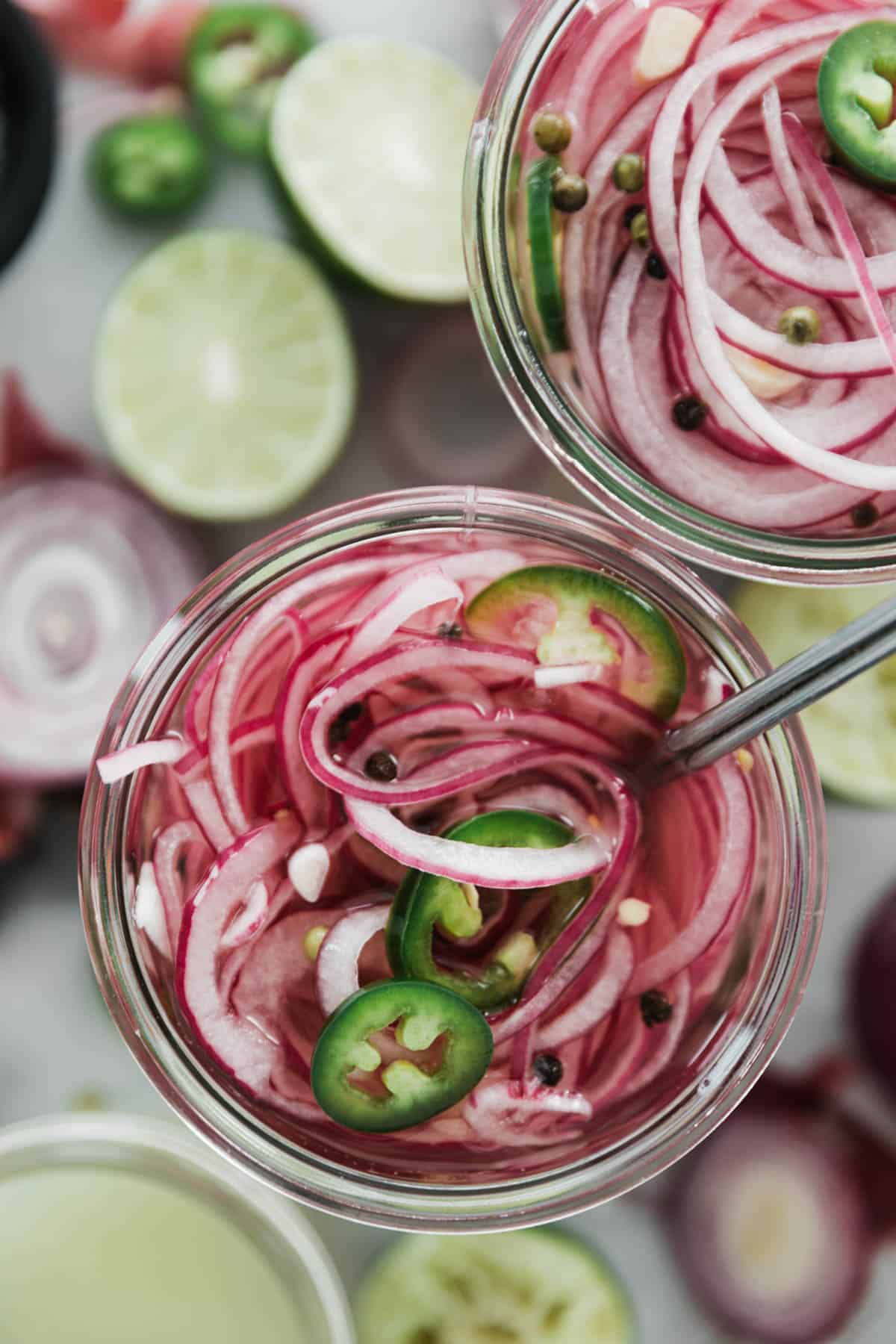 Two jars filled with sliced red onions vinegar, spices and sliced jalapeños.