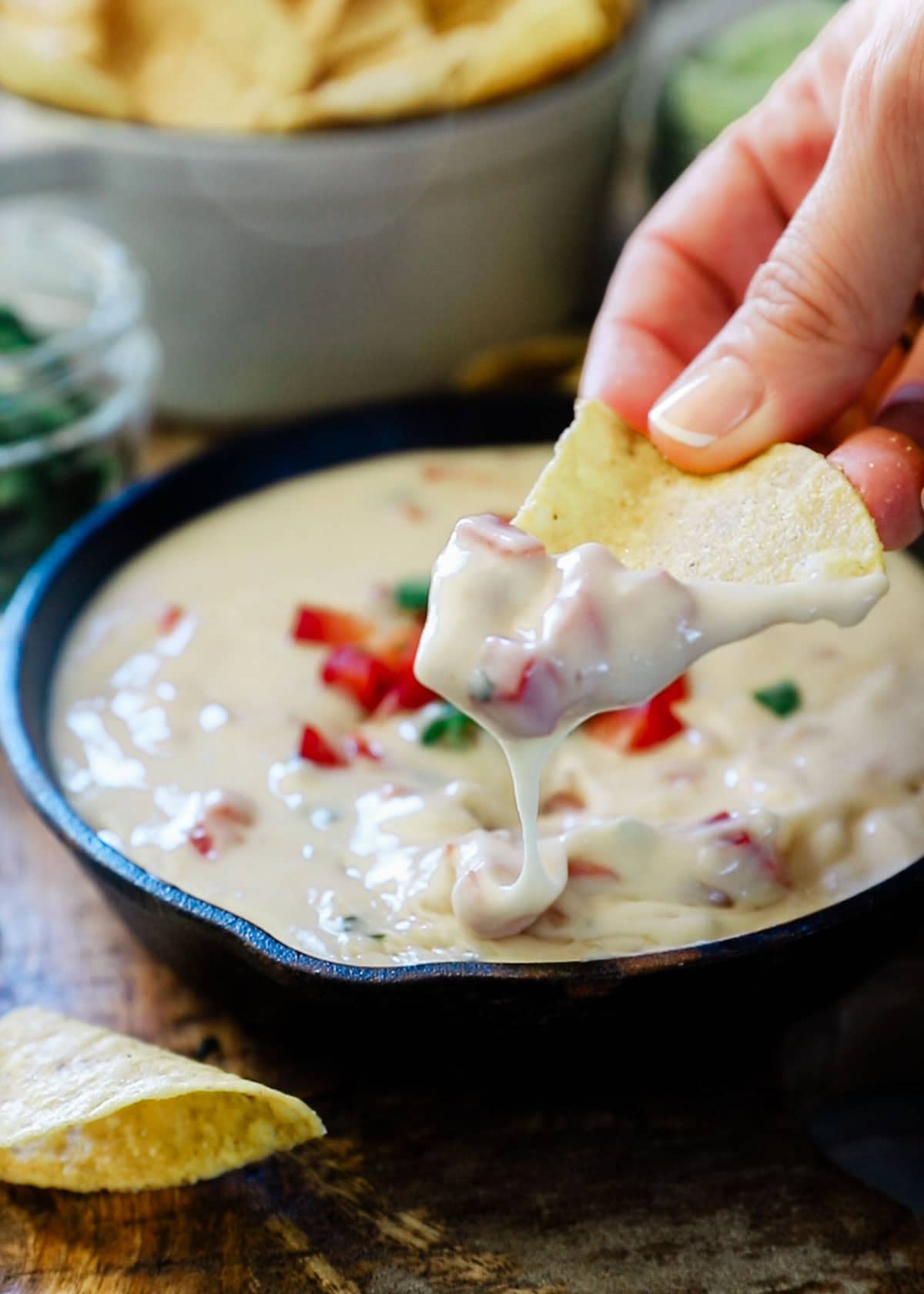 Queso blanco dip being scooped out of a cast iron skillet with a tortilla chip.