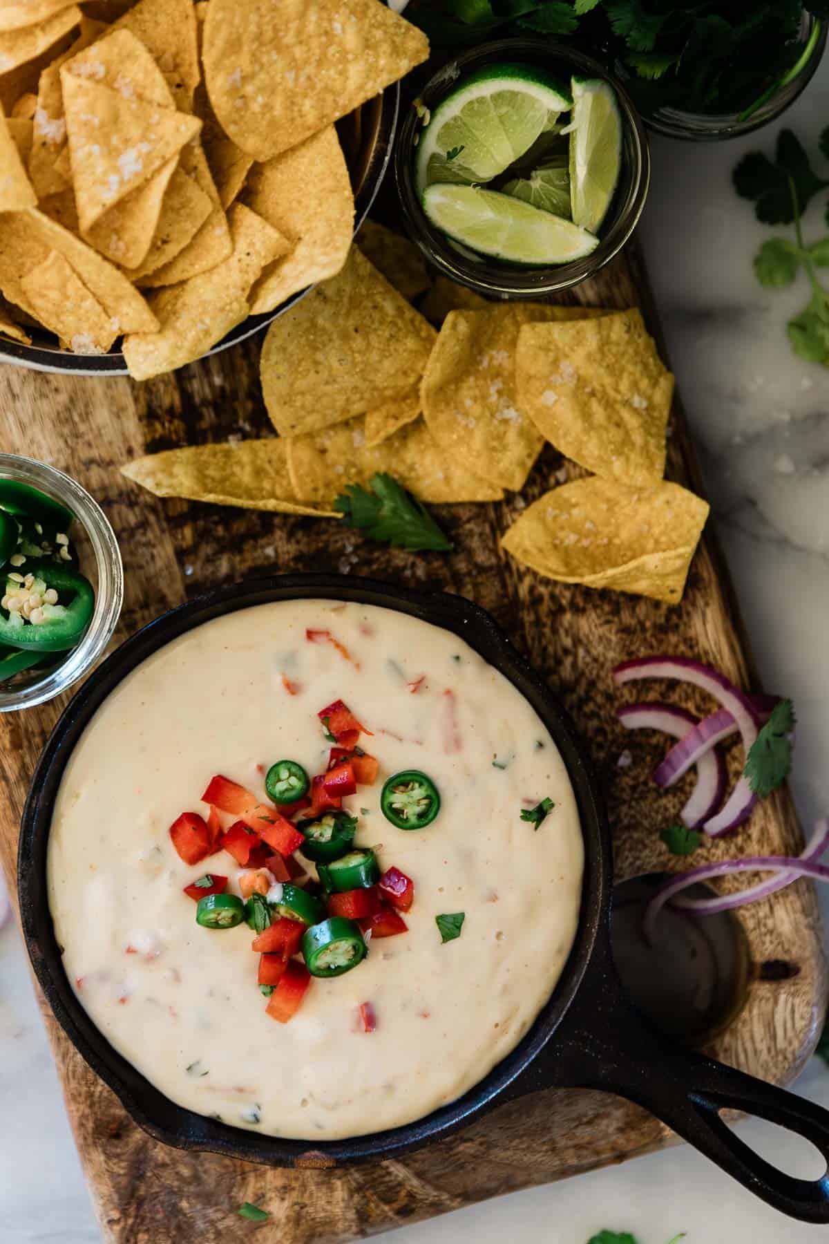 Queso blanco in a cast iron skillet. It atop a wooden cutting board with tortilla chips.