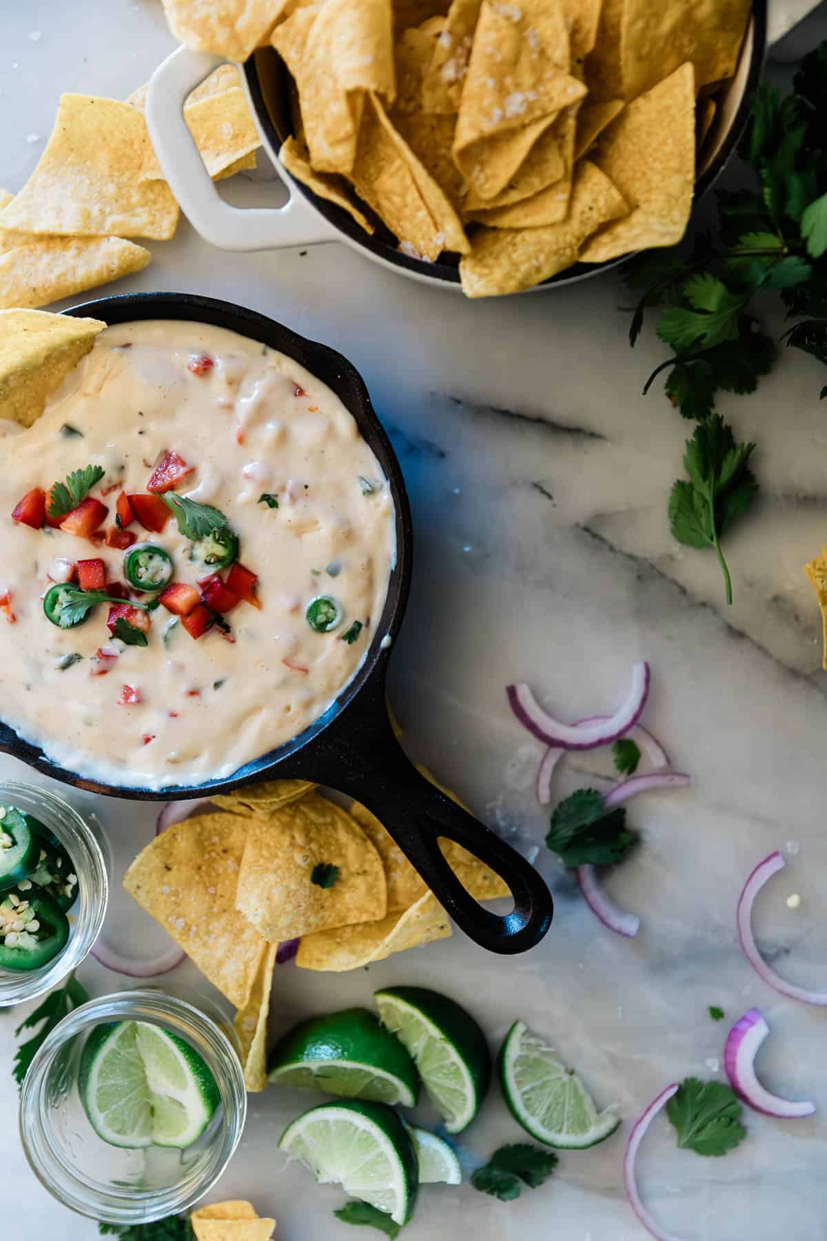 Queso blanco Mexican cheese dip in a small cast iron skillet. It is set on a marble counter and surround by chips.