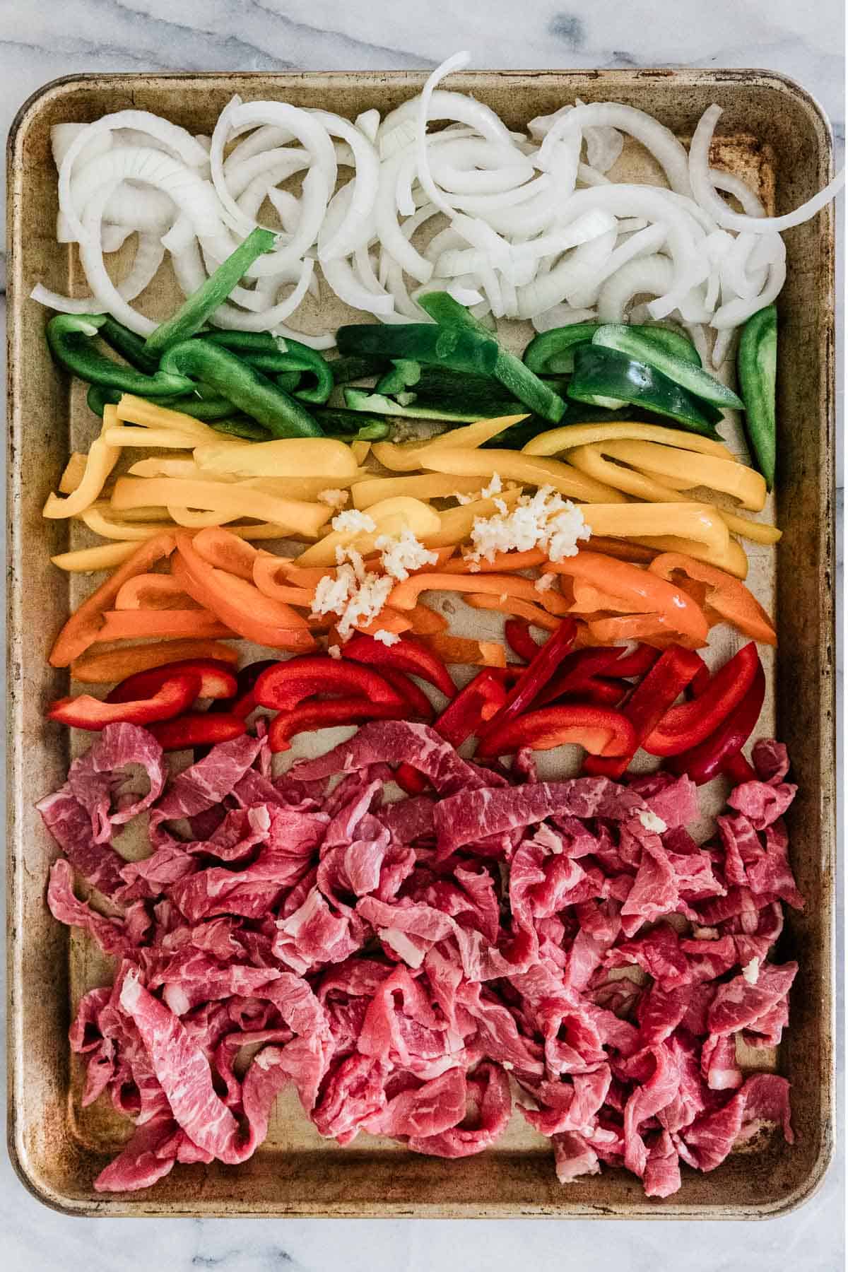 Onions, bell peppers, and steak on a sheet pan.