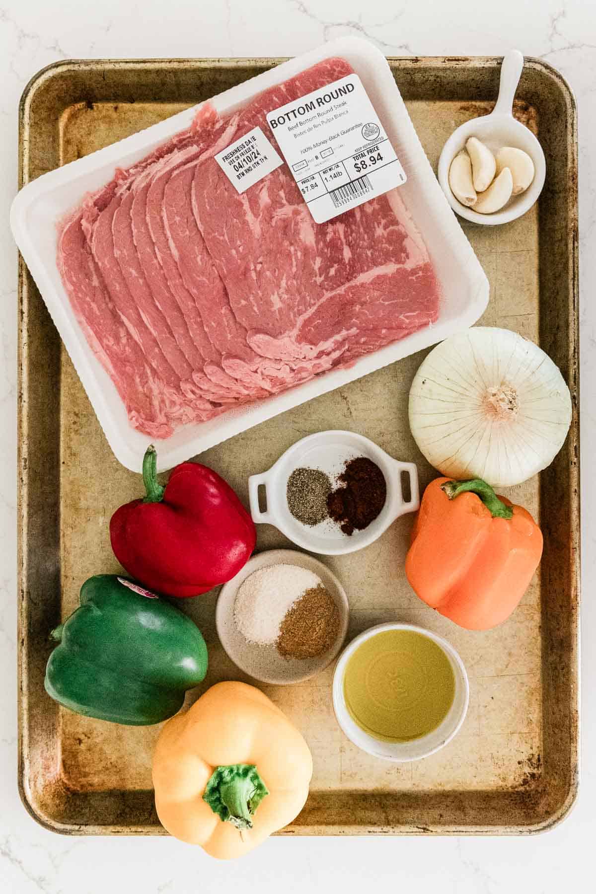 Steak, bell peppers, onion, olive oil and seasoning on a sheet tray.