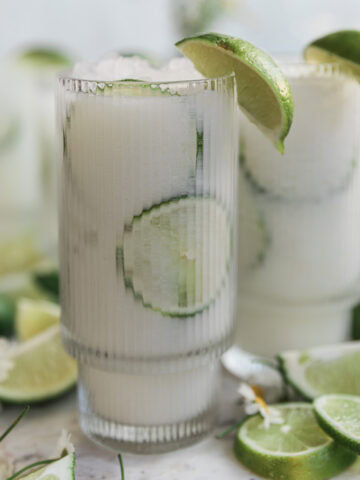 Brazilian lemonade in a tall glass garnished with lime wedges.