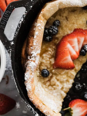 Fluffy German pancake in a cast iron pan with blueberries, strawberries and powder sugar.