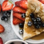 Slice of German pancake with blueberries, strawberries and a dusting of powder sugar and syrup.